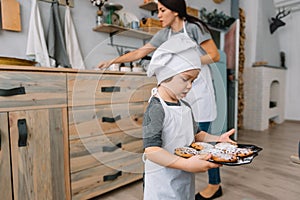 Young happy mom and her baby cook cookies at home in the kitchen. Christmas Homemade Gingerbread. cute boy with mother in white