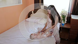 Young happy mom is playing with a newborn baby in the bedroom on the bed.