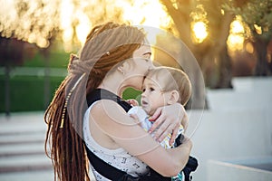 Young happy mother with baby son in ergo backpack walking in Sunny summer day. Concept of the joy of motherhood