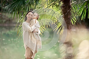 Young and happy mother cares for her young son, and walks along the shore of the lake in the summer in the park