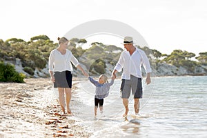 Young happy mother and father walking with little daughter on beach in family vacation concept