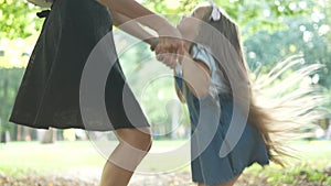 Young happy mother with her little daughter jumping together having fun in green summer park.