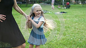 Young happy mother with her little daughter jumping together having fun in green summer park.