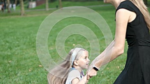 Young happy mother with her little daughter jumping together having fun in green summer park.