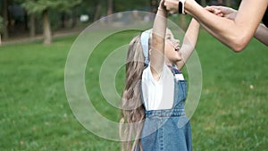 Young happy mother with her little daughter jumping together having fun in green summer park.