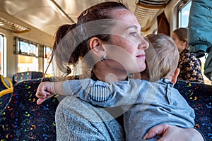 Young happy mother holding baby while he pulls her hair while travelling by train