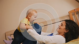 Young Happy Mother Holding her Newborn Child and throws up. Family at home. Beautiful smiling Mom and Happy Baby