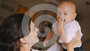 Young Happy Mother Holding her Newborn Child and throws up. Family at home. Beautiful smiling Mom and Happy Baby