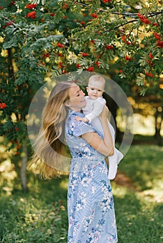 A young happy mother holds her baby son in her arms against the background of Rowan branches with berries, they are cheerfu