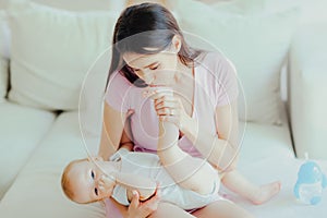 Young happy mother kisses the feet of her little baby