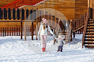 A young happy mother and a little girl in warm outerwear walk in the park in the playground in winter. beautiful woman and baby in