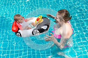 Young happy mother in a pink bikini having fun and catch baby in the pool. A joyful little child sits in an inflatable boat in the