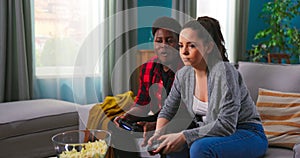 Young happy multinational couple sitting at home on couch and playing video games on console.