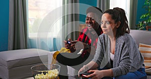 Young happy multinational couple sitting at home on couch and playing video games on console.