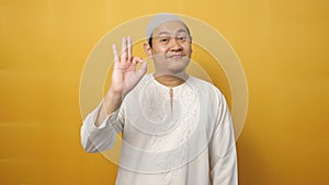 Young happy muslim Asian man smiling while showing okay OK sign hand gesture, against yellow background