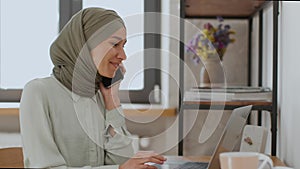 Young happy muslim lady in hijab talking with business partners, discussing documents on laptop, enjoying pleasure talk