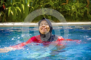 Young happy muslim woman playing with water excited in resort swimming pool splashing and having fun wearing traditional islam
