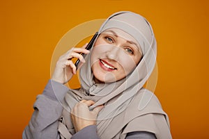 Young happy Muslim Woman Using Mobile Phone standing over yellow background. Free technology lifestyle muslim concept