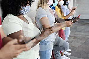 Young happy people using mobile phones while wearing safety masks outdoor - Focus on center girl