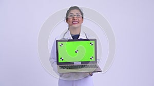 Young happy Persian woman doctor showing laptop and looking surprised