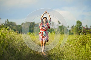 Young happy and playful Asian Chinese woman in beautiful dress having fun enjoying holidays excursion on grass tropical field smil