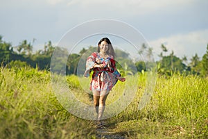 Young happy and playful Asian Chinese woman in beautiful dress having fun enjoying holidays excursion on grass tropical field smil