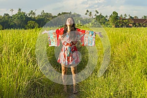 Young happy and playful Asian Chinese woman in beautiful dress having fun enjoying holidays excursion on grass tropical field smil