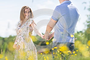 Young happy pregnant couple in love holding hands, relaxing in meadow.