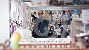 A young happy pregnant woman chooses clothes for a newborn in a children`s store