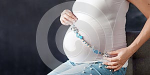 Young happy pregnant woman  holding children`s beads. Close up on pregnant belly. Woman expecting a baby. Newborn baby booties in