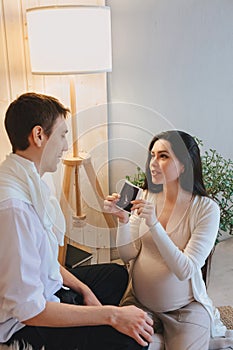 Young happy pregnant woman holding pregnancy ultrasound, showing sonogram picture to pleasantly surprised husband crying from