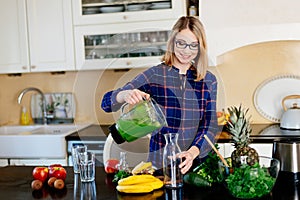 Young happy pregnant woman pouring green smoothie to glass cup