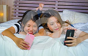 Young happy and pretty Asian Chinese girlfriends sitting at home bedroom laughing and talking having fun using internet social