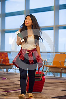 Young happy and pretty Asian Chinese tourist woman pulling suitcase trolley in airport departure gate walking and holding boarding