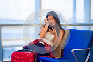 Young happy and pretty Asian Chinese tourist woman sitting at airport departure boarding gate waiting for flight using internet on