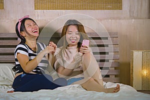 Young happy and pretty Asian Korean girlfriends sitting at home bedroom laughing and talking having fun using internet social