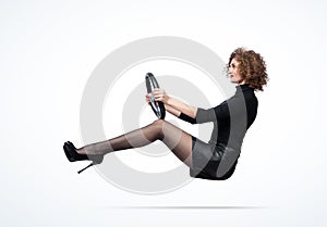 Young happy pretty girl in a black turtleneck, leather skirt with high heels, rides a car holding the wheel. On light background photo