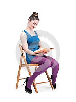 A young happy pretty girl in a mini dress is sitting on a chair and smiling reading a book, isolated on a white