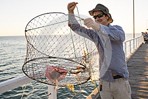 Proud attractive fisherman showing fish and crabs basket net captures smiling at sea dock sunset in man fishing as weekend hobby