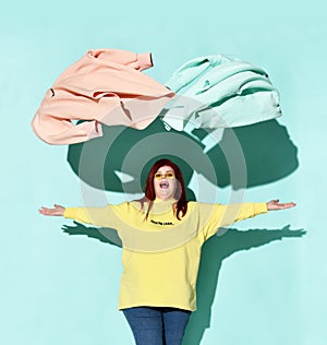 Young happy red haired overweight woman in yellow hoodie and blue jeans throws up out blue and pink clothes