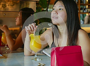 Young happy and relaxed Asian Korean tourist woman drinking healthy orance juice at hotel cafe or restaurant resort smiling