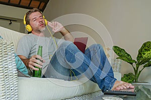 Young happy relaxed and attractive man sitting at home sofa couch with headset and laptop listening to internet music online enjoy