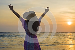 Young happy and relaxed woman in Summer hat looking at the sun over the sea during an amazing beautiful sunset at tropical paradis