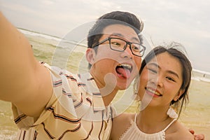 Young happy and romantic Asian Chinese couple in love enjoying holiday taking selfie photo together on beautiful beach having fun