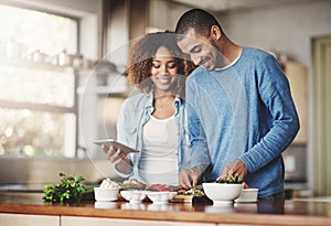 Young, happy and romantic couple cooking healthy food together following recipes online on a tablet. Smiling husband and