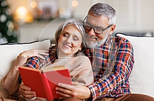 Young happy senior family couple in love enjoying Christmas holidays together at home, reading book