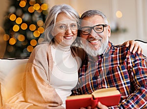 Young happy senior family couple in love enjoying Christmas holidays together at home, reading book