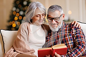 Young happy senior family couple in love enjoying Christmas holidays together at home, reading book