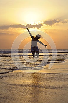 Young happy Asian woman in bikini jumping excited on sunset beach having fun