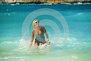 Young happy and sexy blond woman in bikini playing with waves in the sea at stunning beautiful tropical beach enjoying carefree